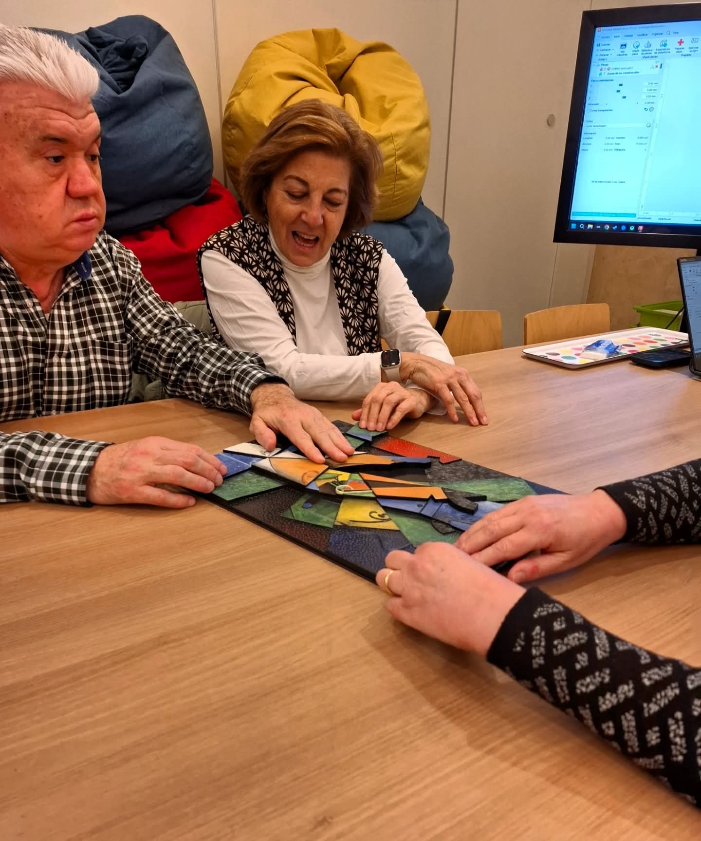 Mujer mayor con gafas observando y tocando una ilustración en blanco y negro sobre una mesa, mientras analiza sus detalles en una sala de reunión.